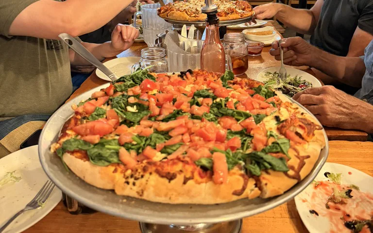 A large pizza surrounded by motorcycle riders at Virginia Creek Settlement.